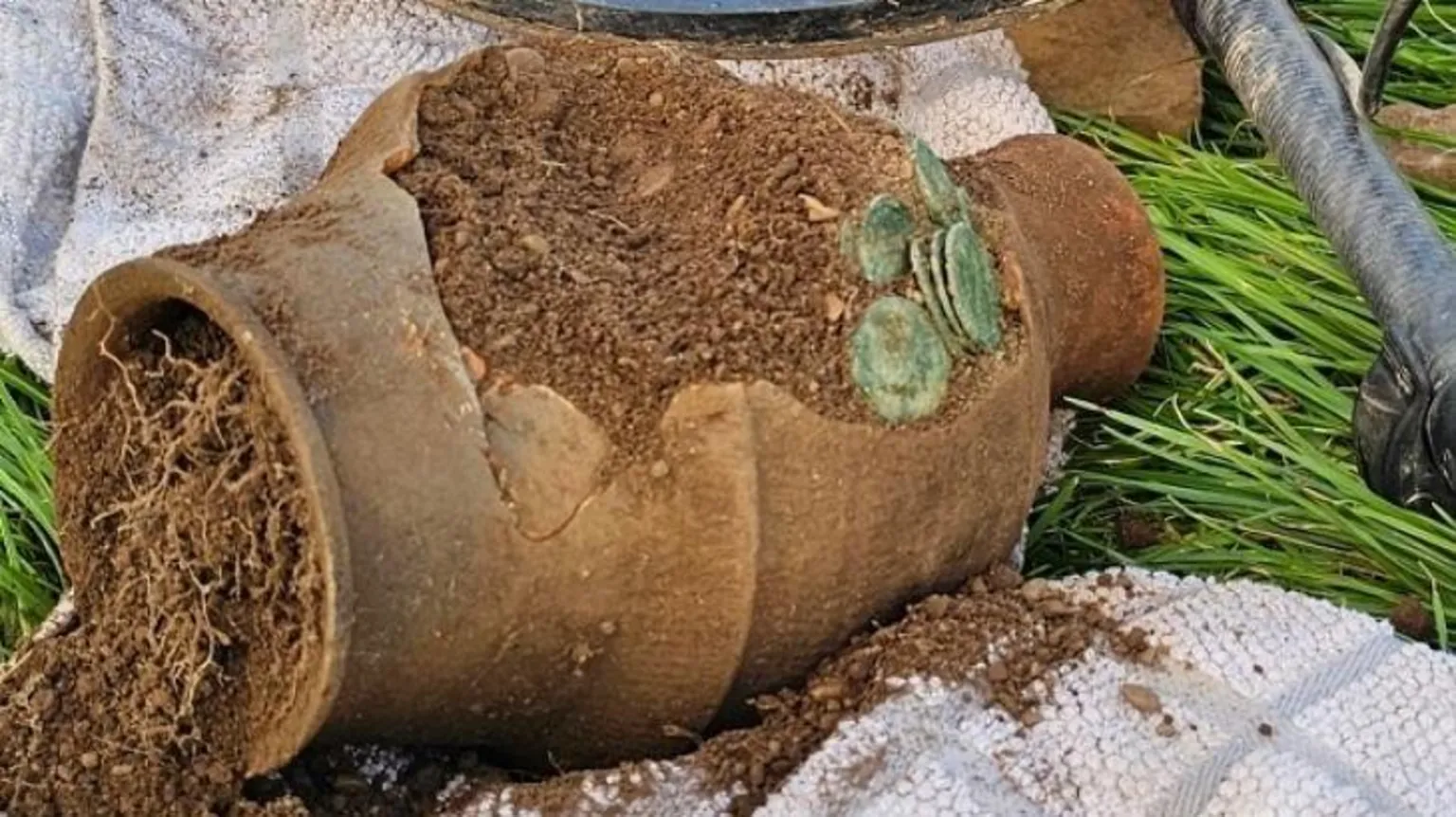 Minelab A clay pot with discoloured coins coming out of it.